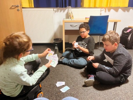 Bild von 3 Schüler*innen beim Kartenspielen.