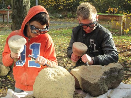 Bild von 2 Schülern, die mit Hammer und Meißel einen Stein bearbeiten.